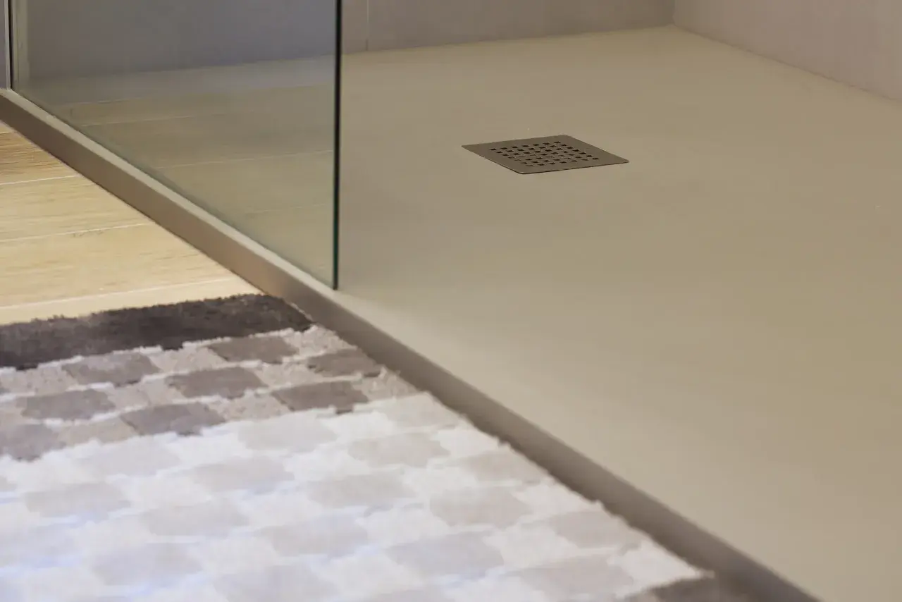 Plato de ducha blanco moderno con desagüe cuadrado. Alfombra a cuadros en primer plano.
