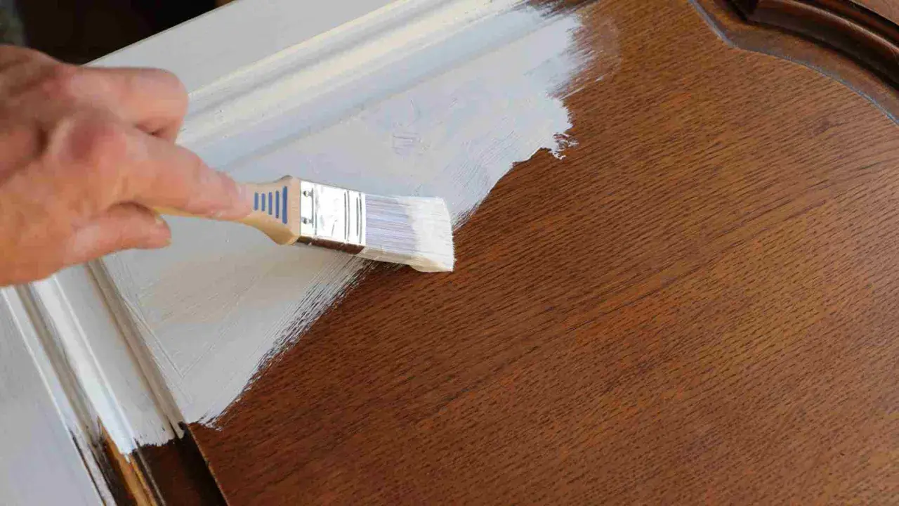 Pintando una puerta de madera ya pintada con brocha y pintura blanca.