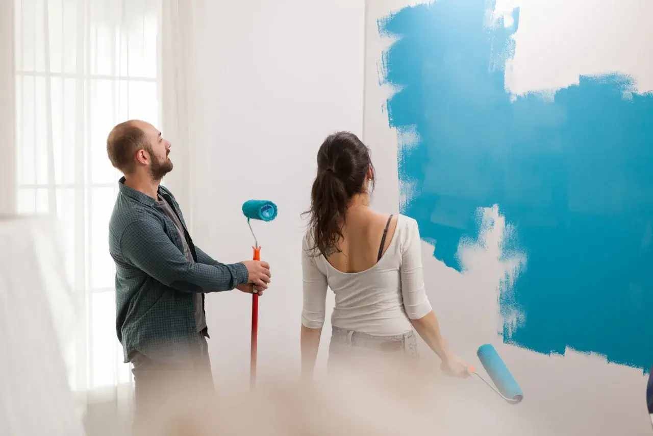 Pareja pintando una pared de azul. Él mira al techo, ella pinta. ¿Qué se pinta primero el techo o las paredes?