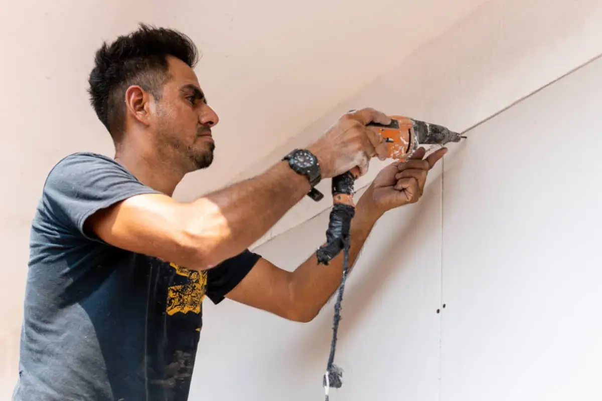 Hombre taladrando una pared de pladur, asegurando la correcta distancia entre perfiles.