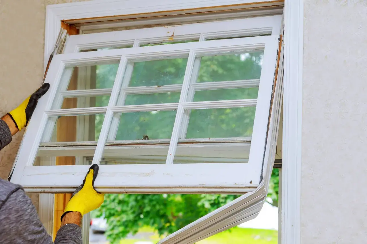 Manos enguantadas retiran un panel de ventana antiguo, imaginando cómo sería cuando se inventó el cristal para las ventanas.