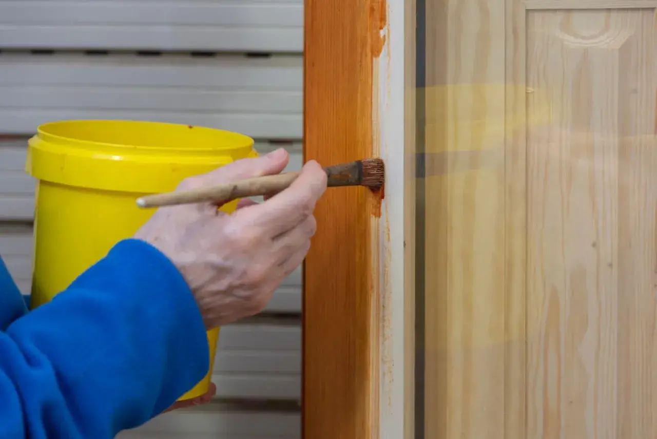 Persona aplica barniz a puertas de madera con brocha.