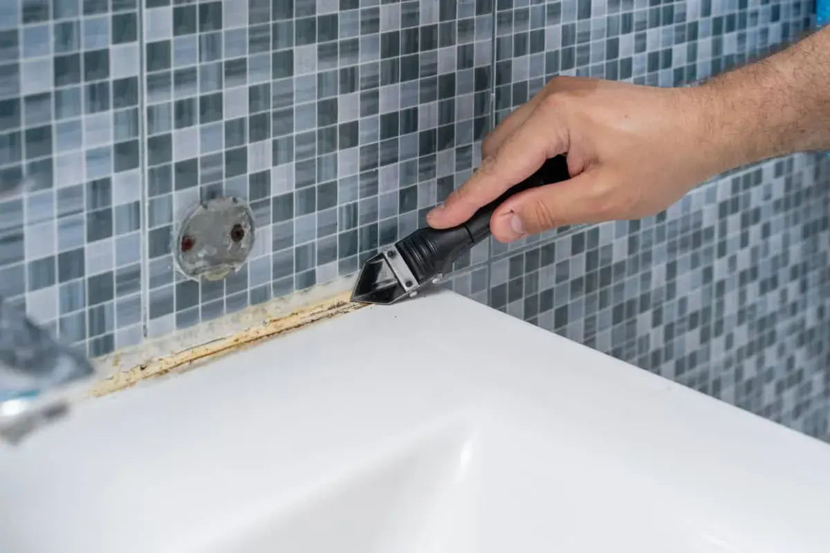 Mano usando herramienta para quitar silicona de plato ducha de resina.