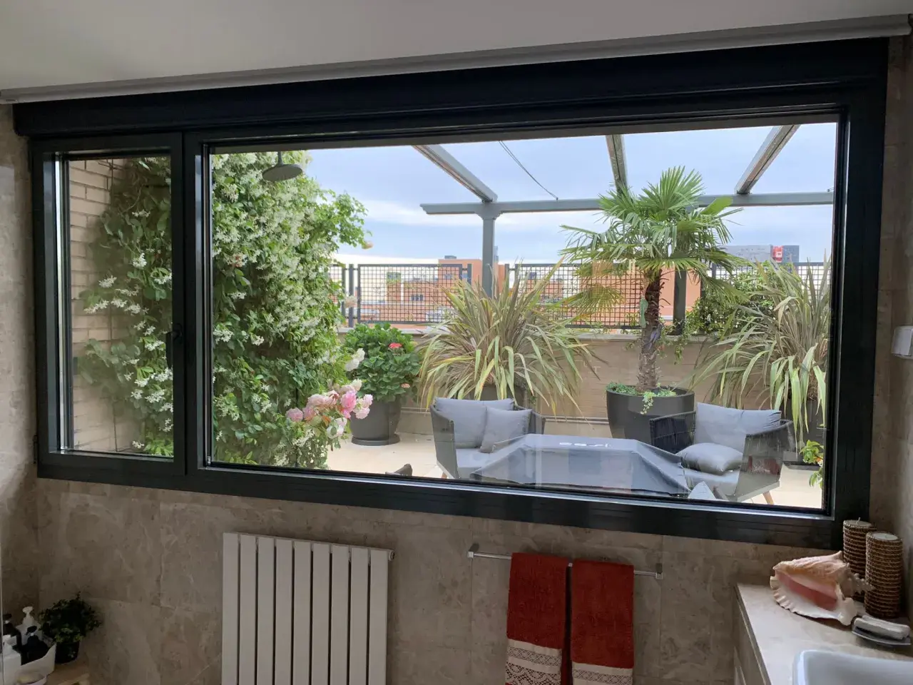 Ventana con perfil de aluminio negro, vista a terraza con plantas y mobiliario. ¿Cual es el mejor perfil de aluminio para ventanas?