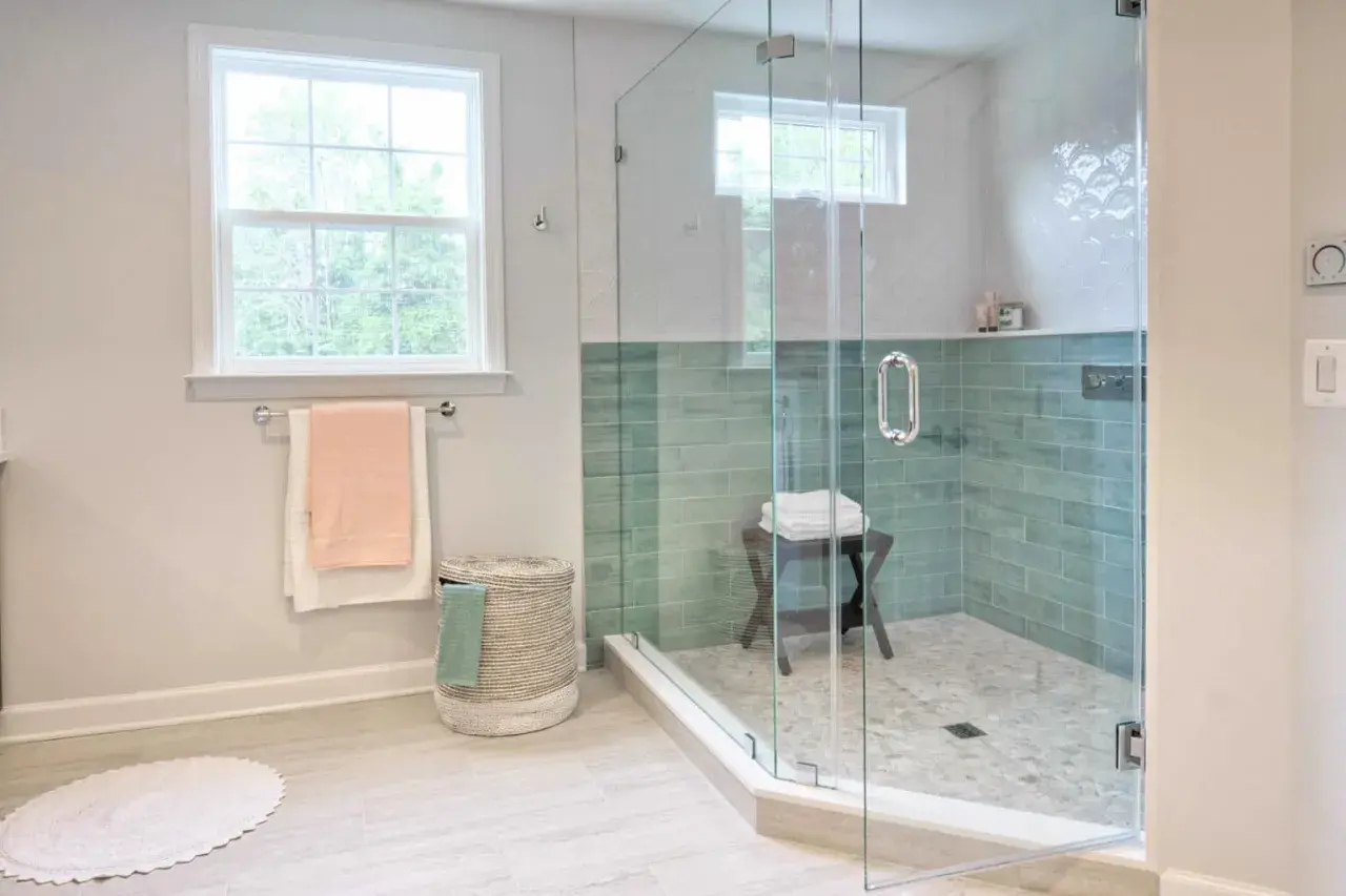 Instalar mampara ducha frontal corredera: baño moderno con ducha de cristal, azulejos verdes y ventana.