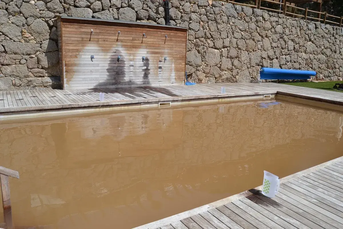 Una piscina de sal con agua turbia y una pared de duchas de madera.