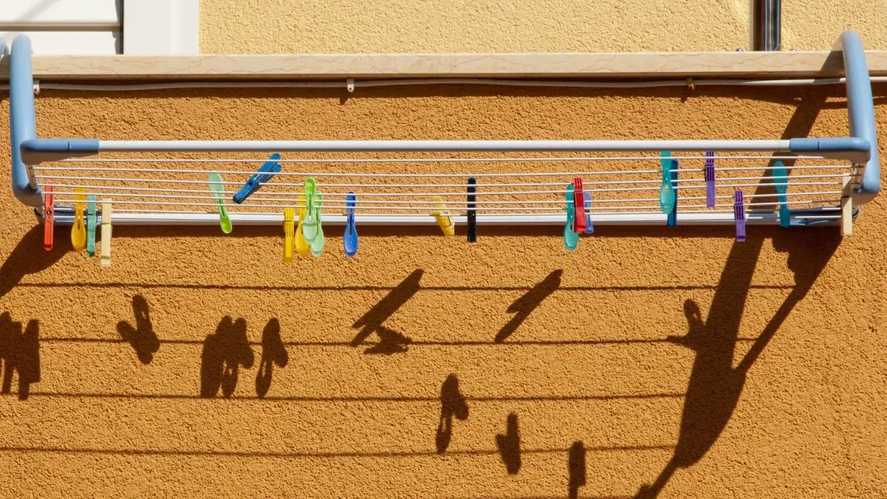 Variedad de pinzas de colores sujetan la ropa en distintos tipos de tendederos exteriores. Las sombras proyectadas crean un patrón interesante.
