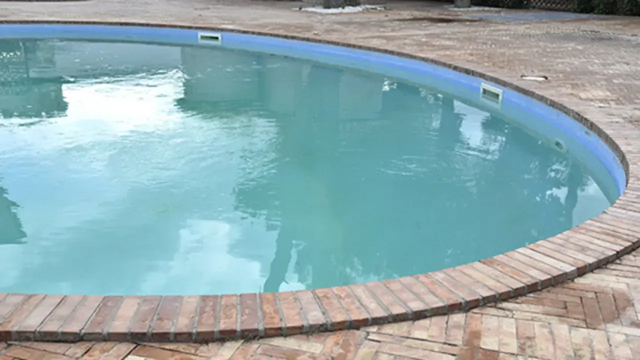 Agua blanca y cristalina en una piscina, rodeada por un borde de ladrillos. El reflejo del cielo en el agua invita a un refrescante chapuzón.