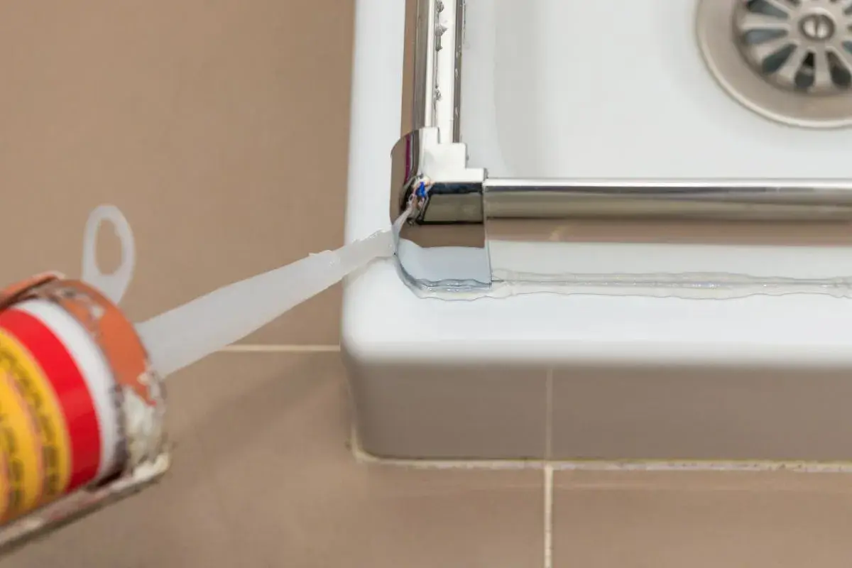 Aplicando sellador para mampara de ducha. Un aplicador de silicona deposita un cordón blanco para sellar la unión entre la mampara y la bañera.