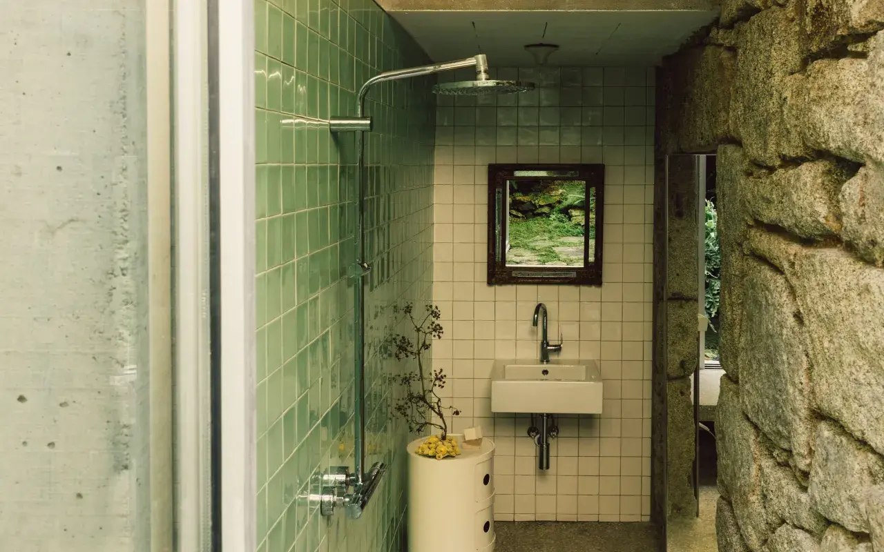 Baños pequeños con ducha, lavabo y espejo con vista a un jardín. Paredes de azulejos verdes y piedra natural.