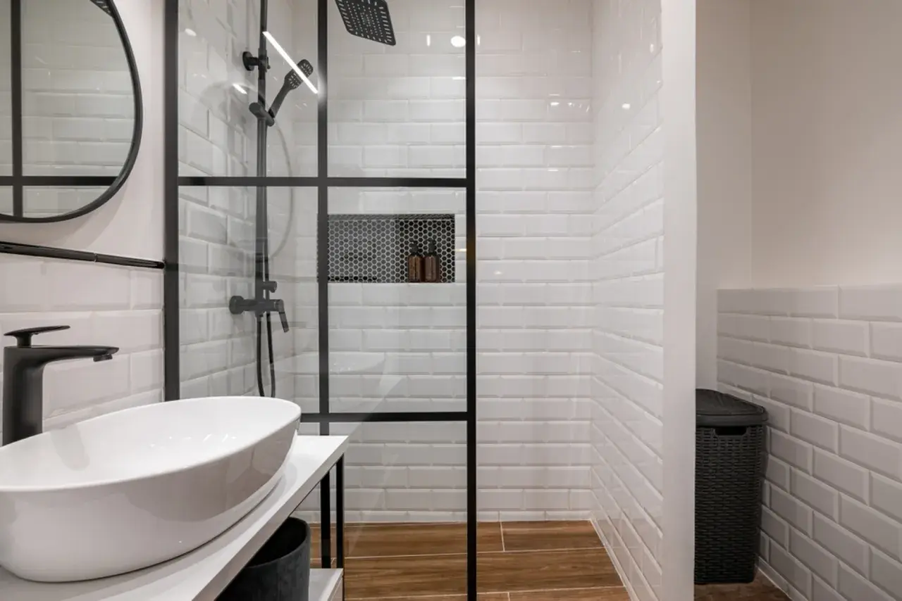 Modern bathroom with a glass-enclosed shower featuring white subway tiles and a built-in niche. The shower is adjacent to a wall, creating a functional space.