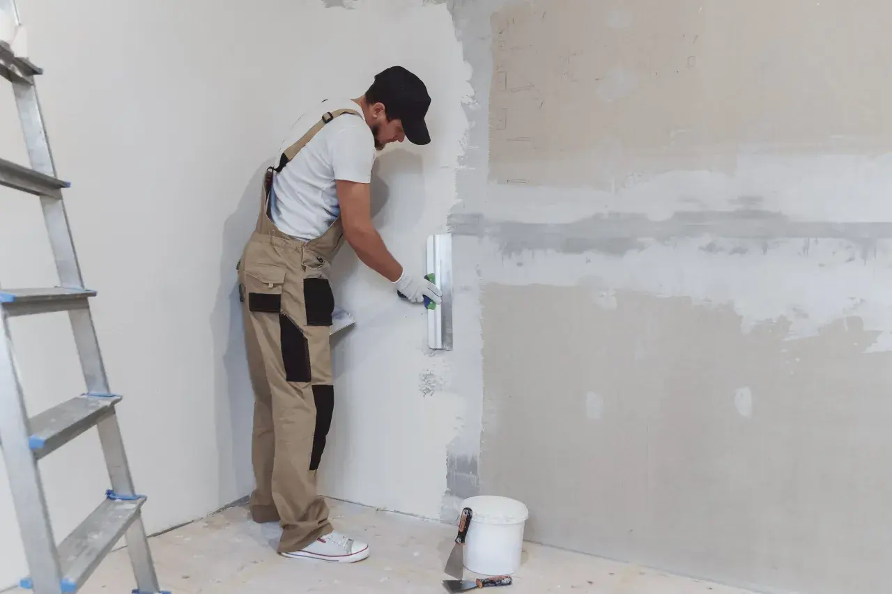 Un obrero aplica yeso a una pared con una llana. Aprende como hacer yeso para renovar tu hogar.