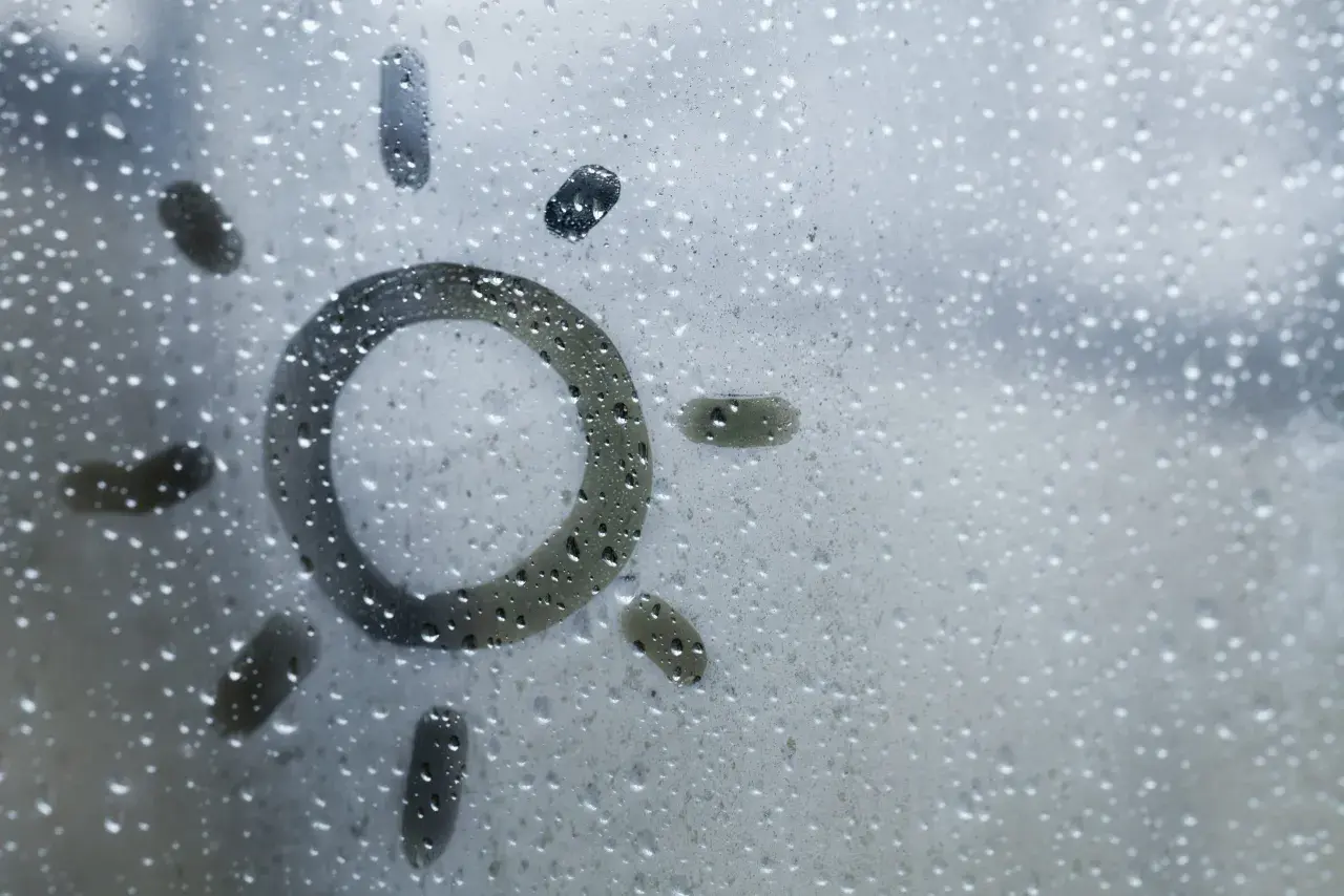Sol dibujado en una ventana con gotas de condensación. Consejos para saber como evitar que las ventanas sudan en invierno.