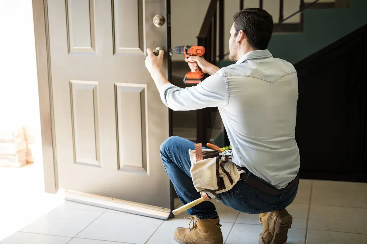 Hombre con taladro y cinturón de herramientas, aprendiendo como desmontar una cerradura de puerta interior.