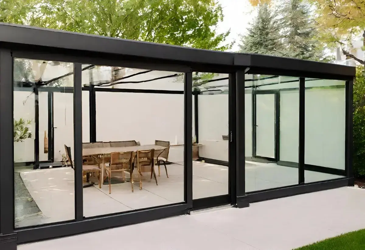 Modernos cerramientos de ventanas de cristal con estructura negra, creando un comedor exterior con mesa y sillas.