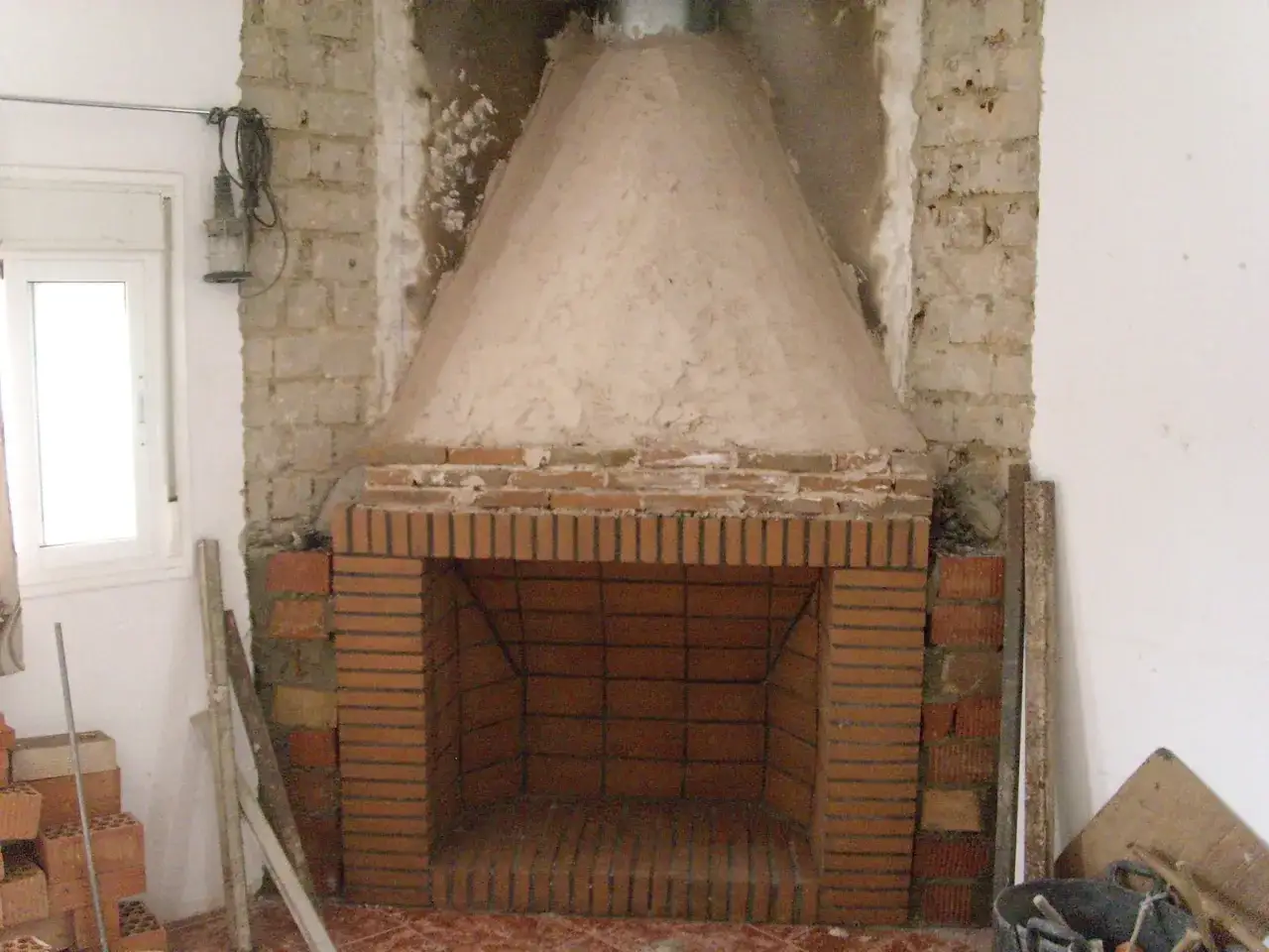 Construcción de chimenea de obra: ladrillos, mortero y campana cónica en proceso.