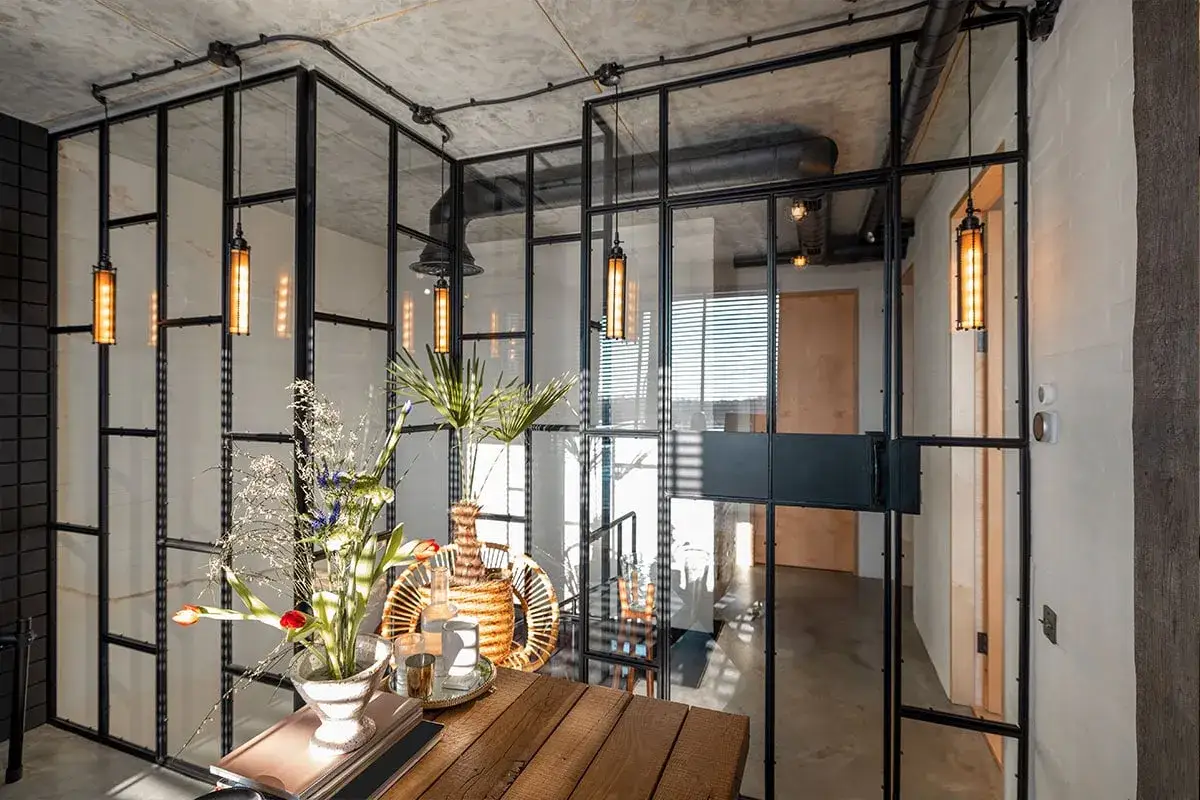 Elegantes tipos de cerramientos interiores de cristal y metal negro, con l&aacute;mparas colgantes y un arreglo floral.