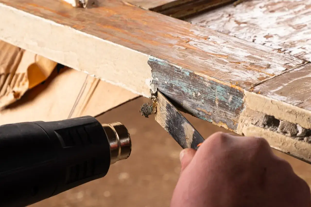 Proceso para quitar la pintura de la madera sin lijar, usando una pistola de calor y rasqueta para remover capas antiguas.