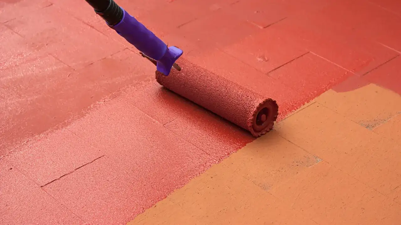 Rodillo pintando suelo de terraza exterior con pintura roja.