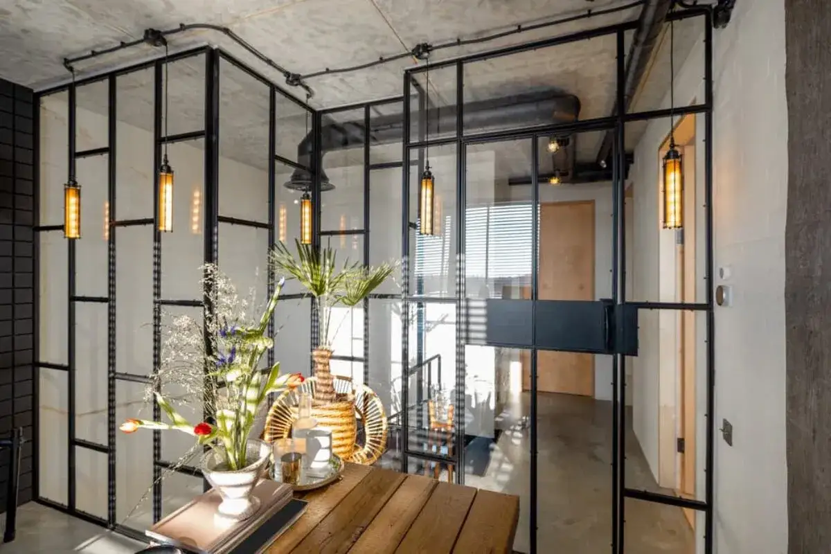 Un espacio moderno con paredes de cristal, l&aacute;mparas colgantes y un arreglo floral sobre una mesa de madera.