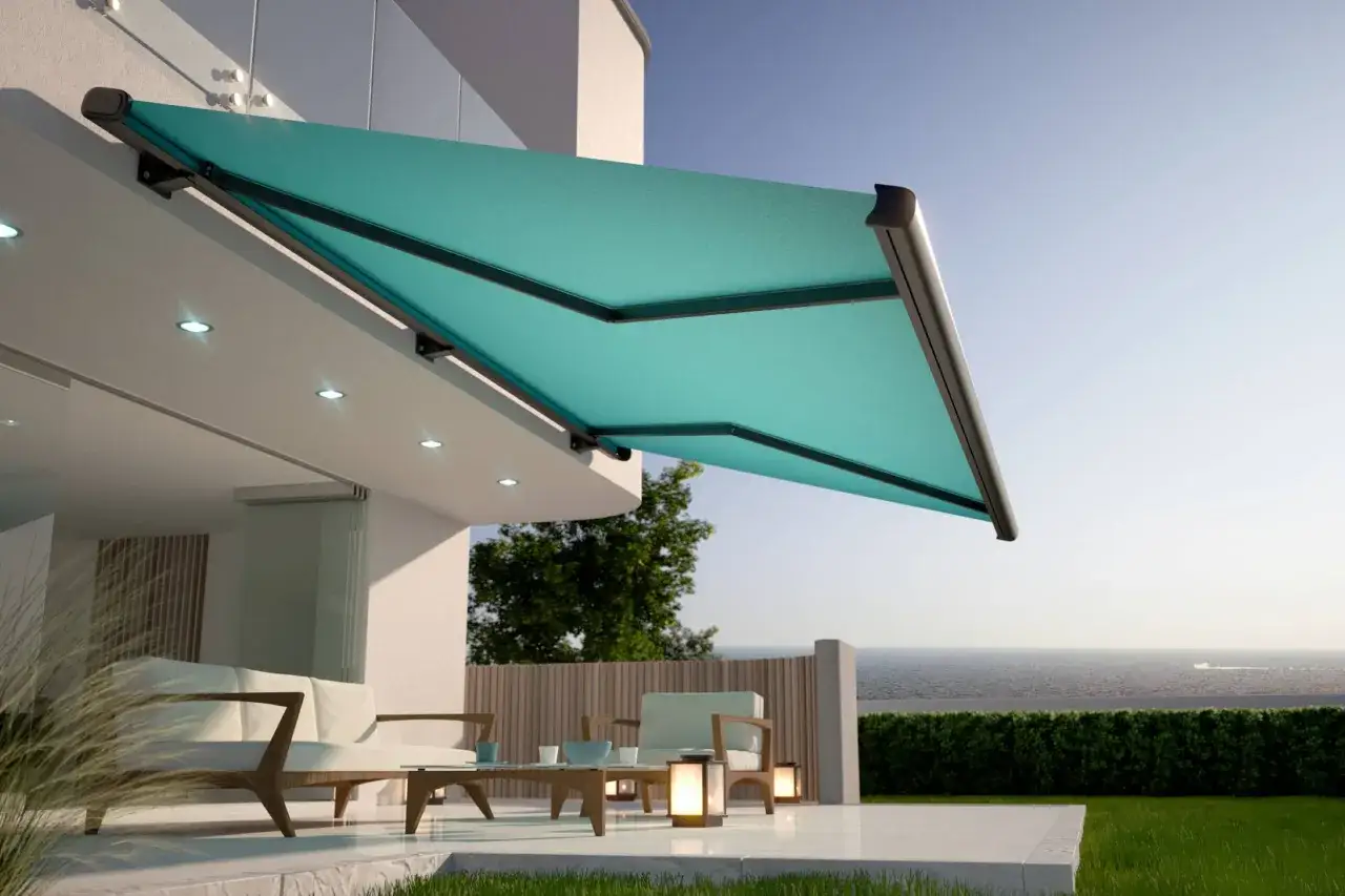Modernos tipos de toldos para patios, con un dise&ntilde;o elegante en color turquesa, protegen un &aacute;rea de descanso con muebles de exterior y vistas al mar.