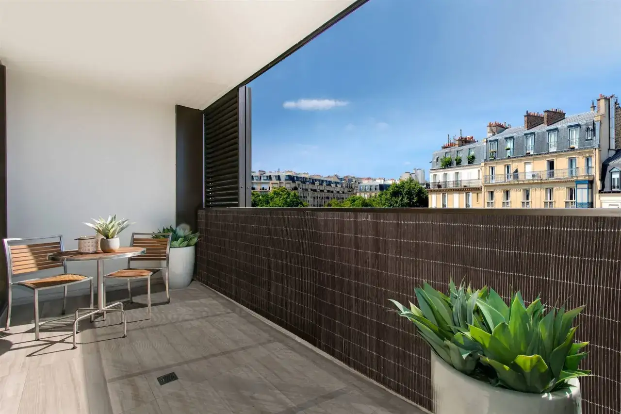 Ideas para cubrir balcones: un set de mesa y sillas en un balc&oacute;n con vistas a edificios parisinos, cubierto con una valla de bamb&uacute;.