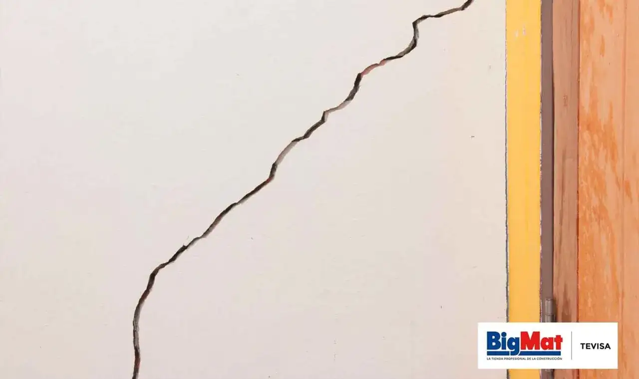 Una grieta profunda en una pared blanca, lista para reparar grietas pared. Junto a un marco amarillo y madera.