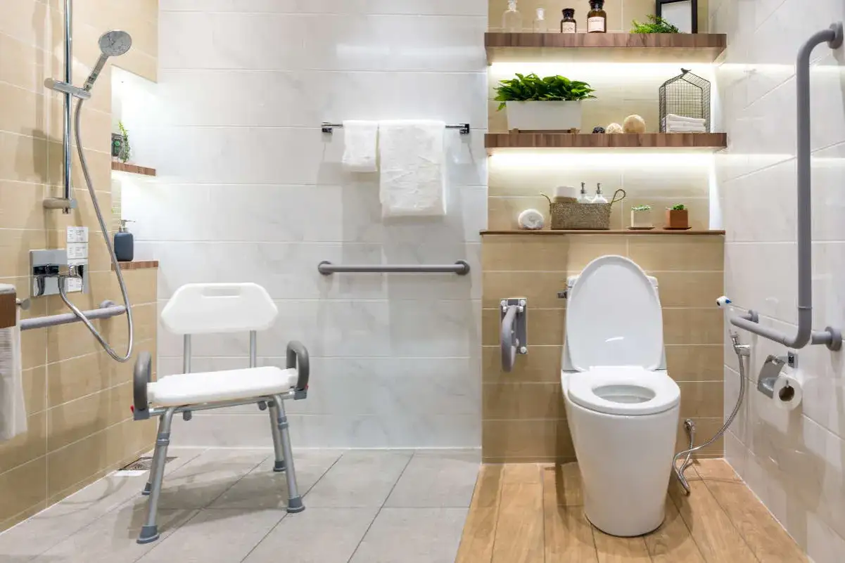 Ba&ntilde;o moderno con duchas adaptadas para personas mayores, silla de ducha, barras de apoyo y WC elevado.