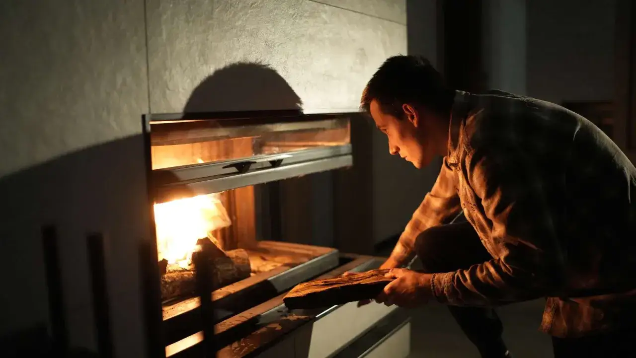 Hombre colocando leña en chimenea moderna para aprovechar su calor.
