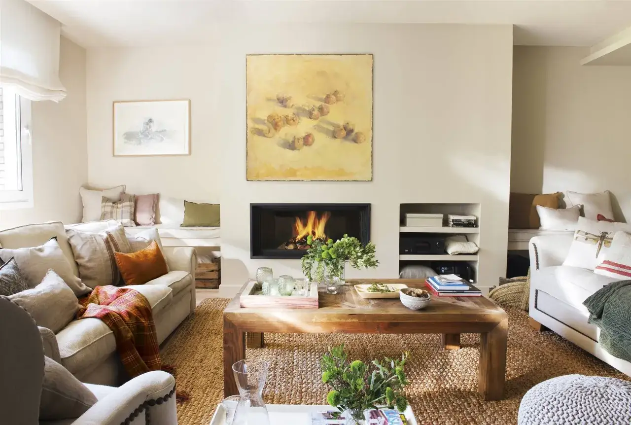 Sal&oacute;n acogedor con chimenea encendida, sof&aacute;s c&oacute;modos y una pintura sobre la beige color pared.