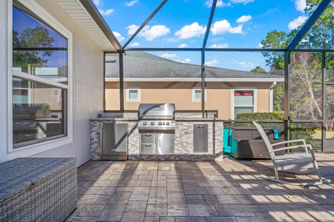 Cocina exterior con parrilla empotrada, refrigerador y varios tipos de cerramientos que protegen del sol y los insectos.