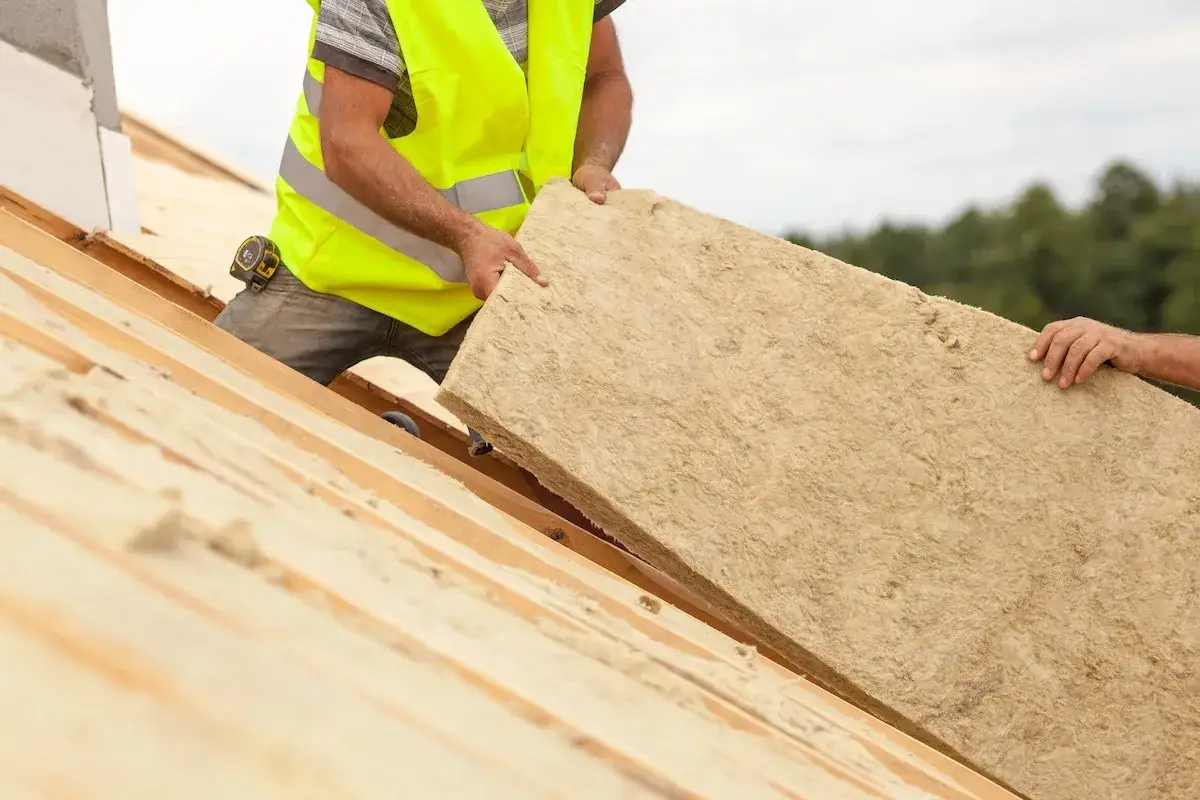 Trabajadores instalan material aislante en un techo de madera. Saben c&oacute;mo aislar un techo del calor para mantenerlo fresco.