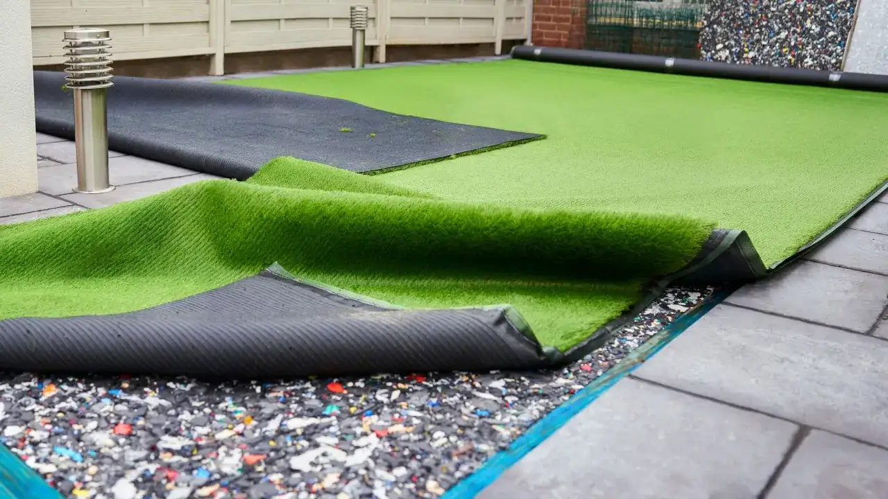 Instalación de césped artificial en terraza. Se ve el rollo de césped desplegado sobre una base de goma y baldosas.