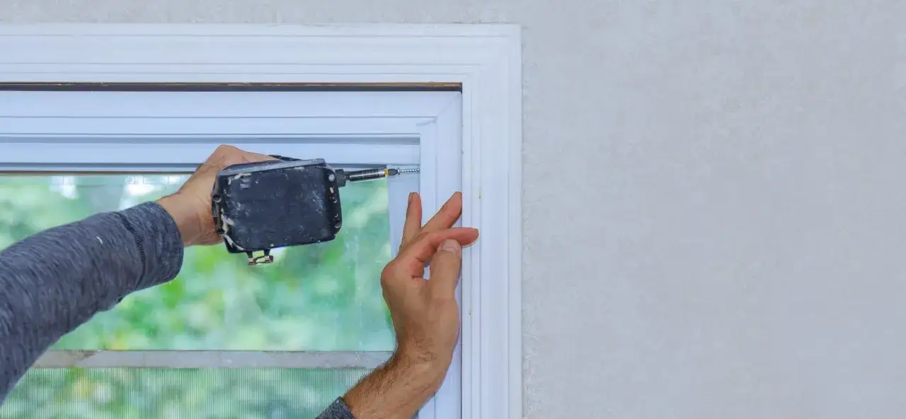 Instalaci&oacute;n de un arreglo de ventanas de PVC. Un trabajador usa un taladro para fijar un marco blanco.