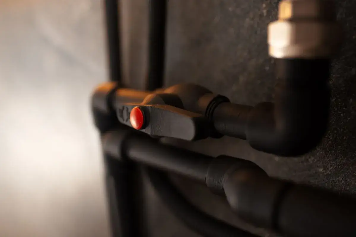 V&aacute;lvula negra con bot&oacute;n rojo, parte de un sistema de tuber&iacute;as. La caldera pierde agua apagada.