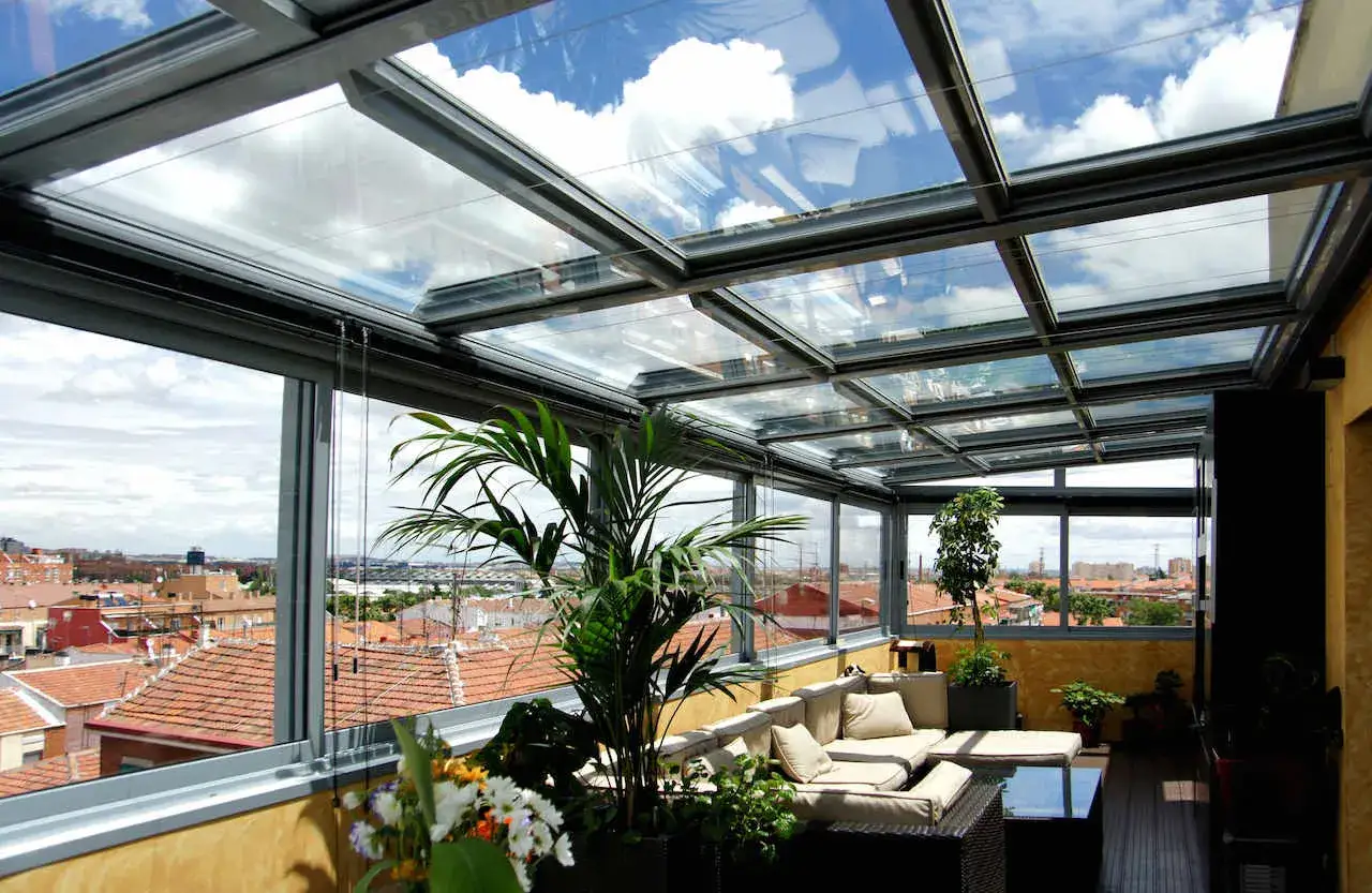 Disfruta de las vistas desde este cerramiento parcial terraza &aacute;tico, con c&oacute;modos sof&aacute;s y plantas bajo un techo de cristal.
