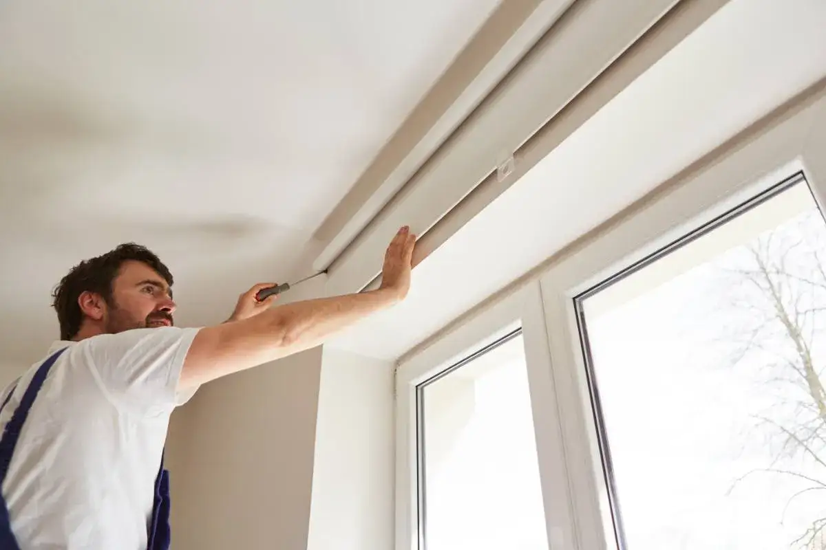 Hombre instala un estor plegable en el techo con un destornillador.