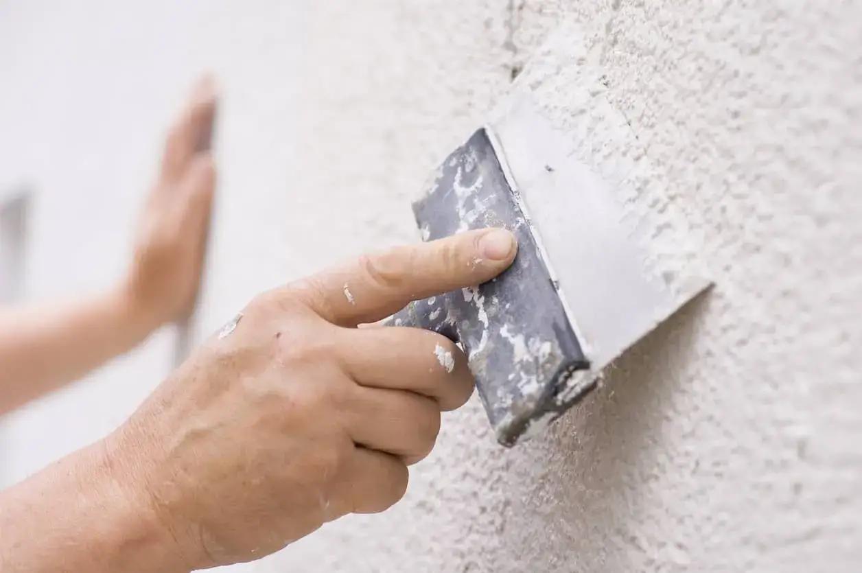 Mano aplicando masa con esp&aacute;tula para reparar gotel&eacute;.