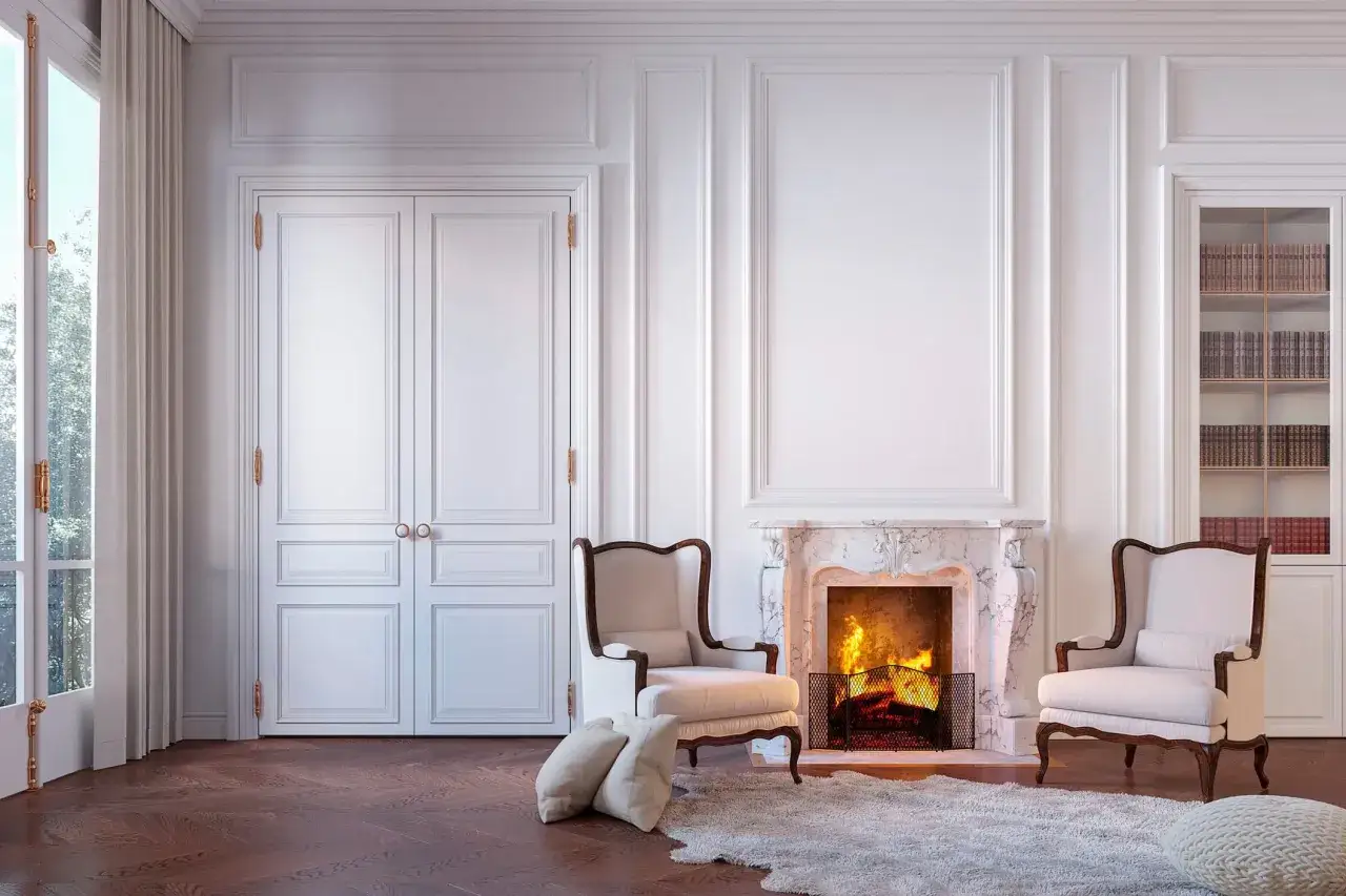 Elegante sal&oacute;n con chimenea encendida, sillones blancos y puertas dobles. Los tipos de blanco en la pintura de la pared crean un ambiente acogedor.