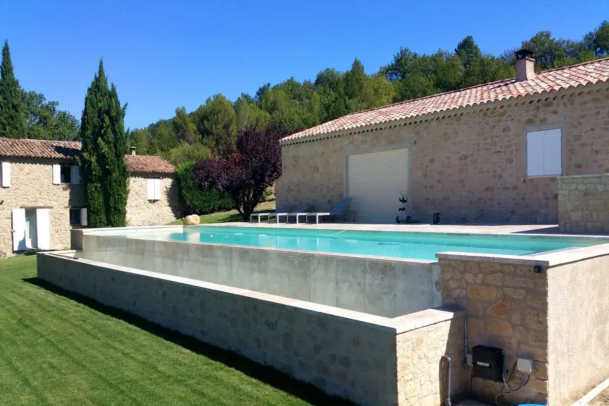 Elegantes piscinas elevadas de obra en cemento, con borde de piedra, junto a una casa rural.