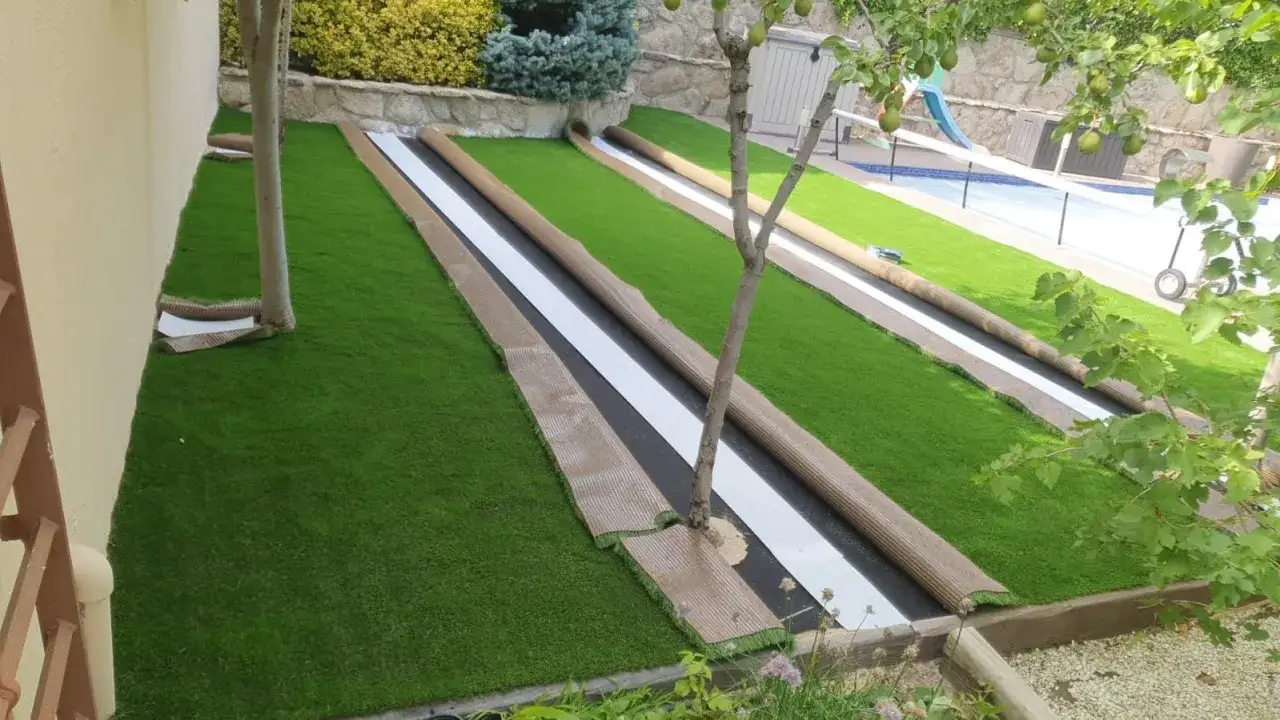 Instalaci&oacute;n de c&eacute;sped artificial en un jard&iacute;n. Rollos de c&eacute;sped listos para pegar, con una piscina al fondo.