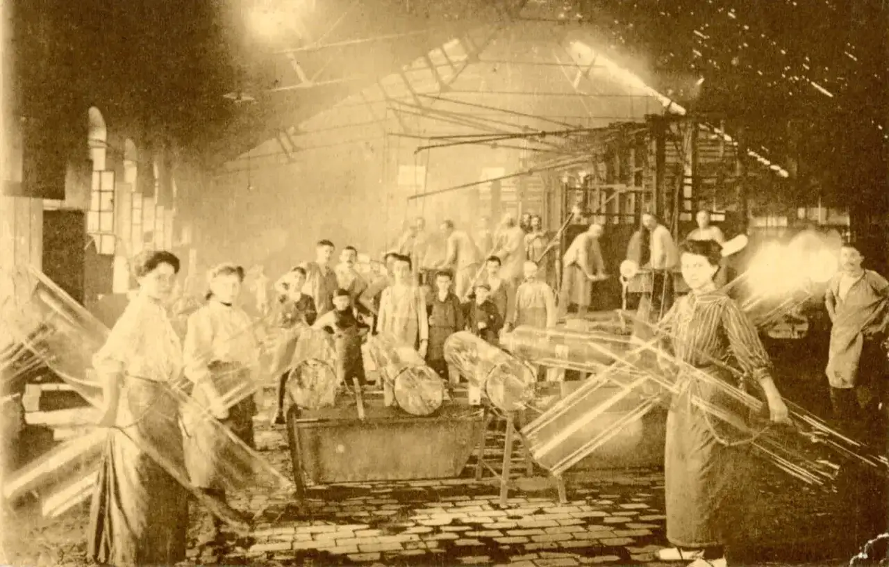 Trabajadores en una f&aacute;brica de vidrio, quiz&aacute;s en la &eacute;poca cuando se invent&oacute; el cristal para las ventanas. Se ven grandes l&aacute;minas de vidrio.