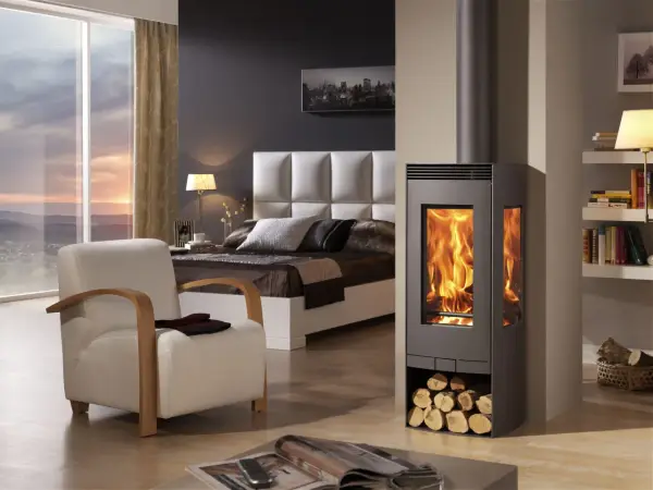 Estufa de leña moderna con fuego encendido, junto a una cama y sillón. Diversos tipos de estufas de gas ofrecen alternativas eficientes.