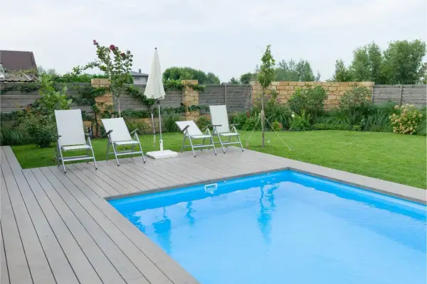 Sillas y sombrilla junto a la piscina, con un suelo de madera que rodea el agua azul.
