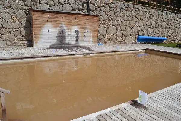 Una piscina de sal con agua turbia y una pared de duchas de madera.