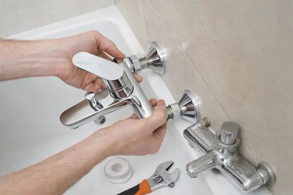 Man installing a new shiny grifo bañera. A wrench and tape are nearby.